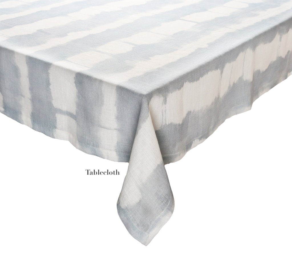 The Kim Seybert Watercolor Stripe White/Blue Linen Collection features a 100% linen rectangular tablecloth with a blue and white pattern and "Tablecloth" printed near the edge—ideal for stylish summer dining.