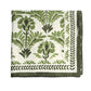 A folded white tablecloth from the Kim Seybert Botanica Tablecloth Collection features a green floral and leaf print, bordered by a green leafy pattern.