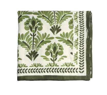 A folded white tablecloth from the Kim Seybert Botanica Tablecloth Collection features a green floral and leaf print, bordered by a green leafy pattern.