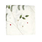 The Christmas Carol Table Linen Collection by Kim Seybert features a folded white embroidered linen napkin with green leaves, pine needles, and red and beige accents—ideal for a festive holiday table.