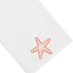 Elevate your home décor with the Haute Home Playful Starfish Bath Collection: a white linen cloth napkin adorned with an embroidered orange starfish in one corner, seamlessly combining elegance and charm.