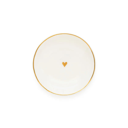 The Sugar Paper Small Round Heart Trinket Tray is a white ceramic dish featuring an elegant gold rim and a delicate gold heart at its center, beautifully photographed on a plain white background to highlight its sophisticated gold details.