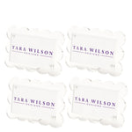 The Scallop Place Card Holder Set by Tara Wilson Designs includes four clear acrylic holders with scalloped edges, each displaying "TARA WILSON DESIGNS" in purple uppercase letters.