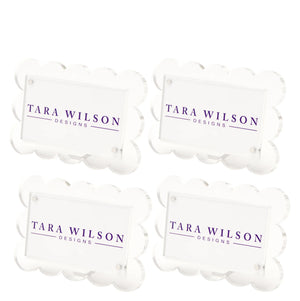 The Scallop Place Card Holder Set by Tara Wilson Designs includes four clear acrylic holders with scalloped edges, each displaying "TARA WILSON DESIGNS" in purple uppercase letters.