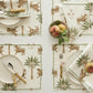 Table set with plates, bamboo-handled cutlery, napkins, and placemats from Matouk’s Tiger Palm Tabletop Collection, featuring jungle motifs with tigers and palm trees, complemented by glasses and a bowl of peaches.