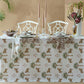The Tiger Palm Tabletop Collection by Matouk features a set for two with a cheetah-print tablecloth, white chairs, bowls, glasses, candles, and a vase with Ottoman florals beside a potted plant and beige jungle-inspired backdrop.