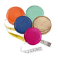 The Graphic Image Leather Tape Measure by Graphic Image comes in orange, blue, mint green, gold, and pink. Each features a hidden button for easy retraction and a yellow-and-white measuring tape for quick measurements anywhere.