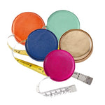 The Graphic Image Leather Tape Measure by Graphic Image comes in orange, blue, mint green, gold, and pink. Each features a hidden button for easy retraction and a yellow-and-white measuring tape for quick measurements anywhere.