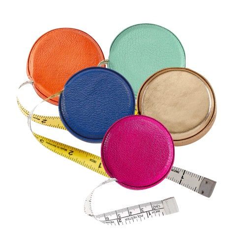 The Graphic Image Leather Tape Measure by Graphic Image comes in orange, blue, mint green, gold, and pink. Each features a hidden button for easy retraction and a yellow-and-white measuring tape for quick measurements anywhere.