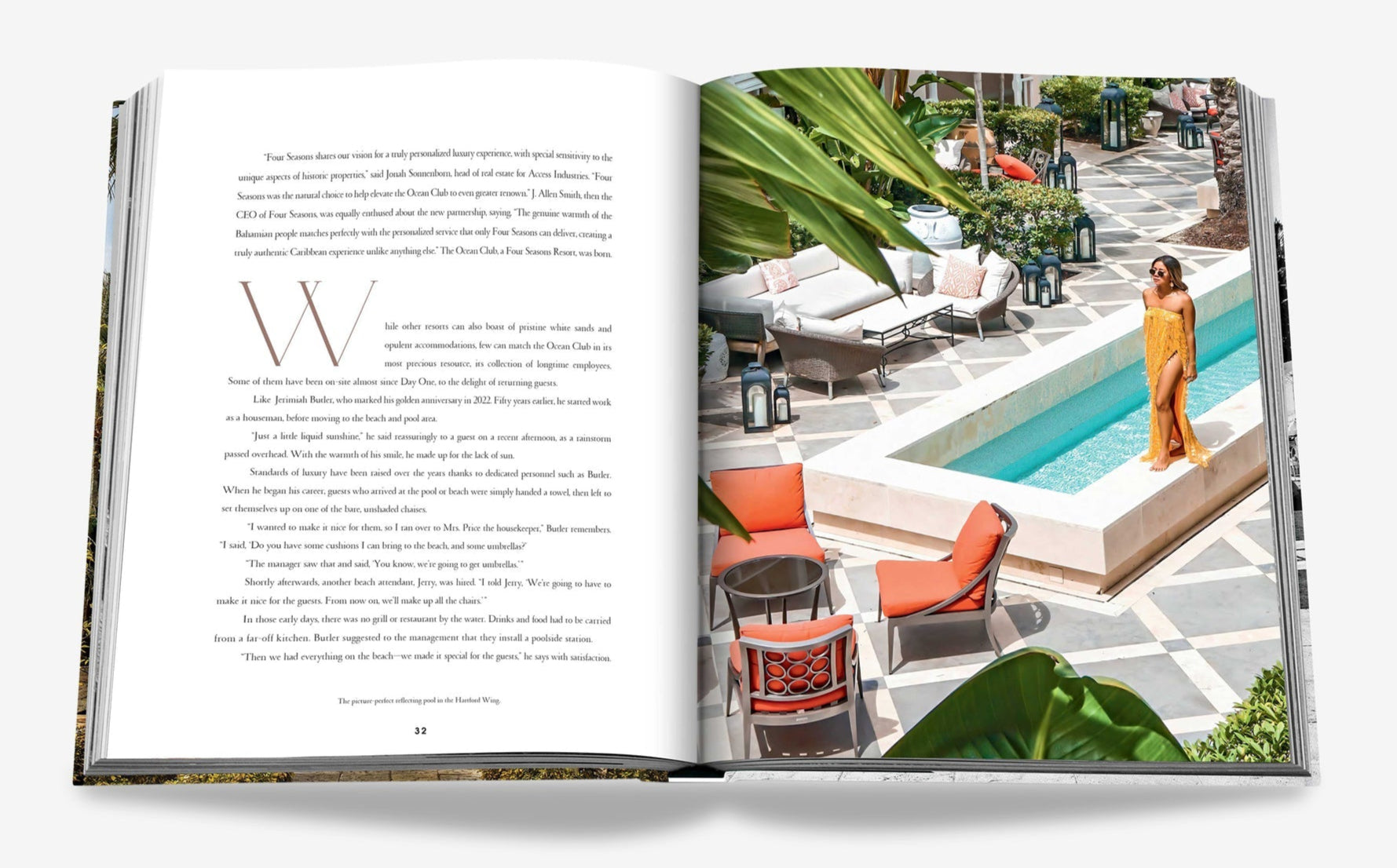 An open book reveals a Bond-like poolside scene from "The Ocean Club" by Assouline, with a woman in an orange dress on the right and text on the left, surrounded by lush plants and elegant outdoor furniture.
