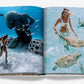 An open book showcases underwater scenes at The Ocean Club, a luxury Bahamian resort: one with a person near a statue amid vibrant fish and another with someone playing with sea turtles. Evoking Bond-like aquatic escapades, it's from the Assouline brand.