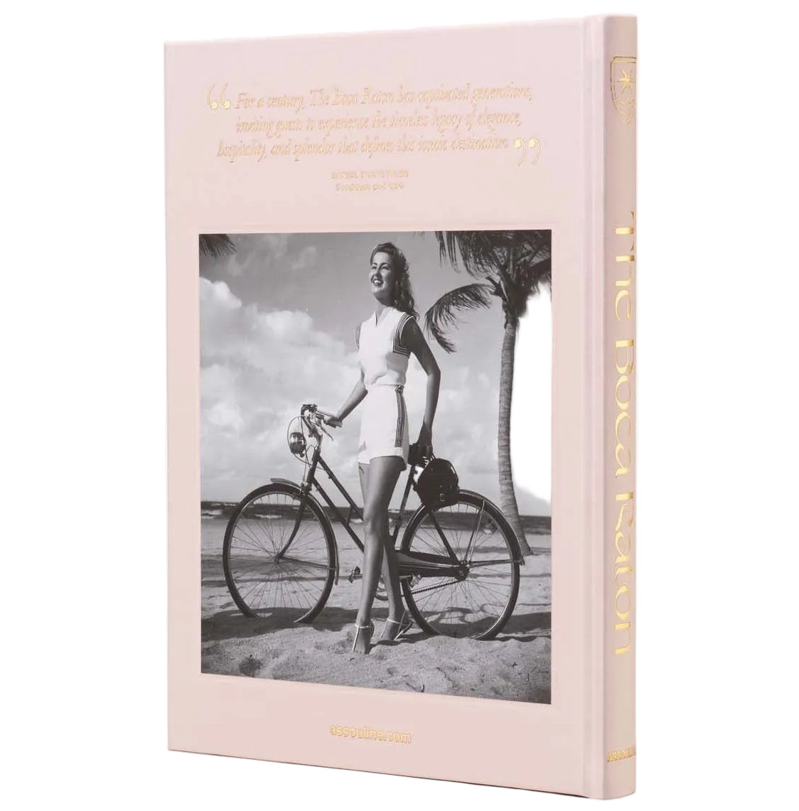 The Boca Raton: A Century of Being Iconic by Assouline features a hardcover with a black-and-white photo of a woman beside a bicycle and gold spine lettering, celebrating the legacy of the famed luxury resort.