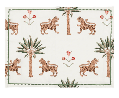 The Matouk Tiger Palm Tabletop Collection features a rectangular placemat adorned with Schumacher's jungle motif—tigers, palm trees, and red flowers—set on a white background with a green border.