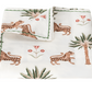 The Matouk Tiger Palm Tabletop Collection, featuring folded white fabric with tiger, palm tree, and Ottoman floral illustrations, offers luxury with Schumacher design and meets the OEKO-TEX Standard 100 for ecological and safe textiles.