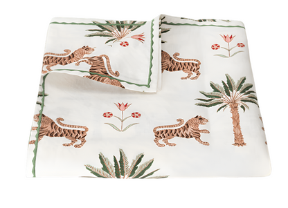 The Matouk Tiger Palm Tabletop Collection, featuring folded white fabric with tiger, palm tree, and Ottoman floral illustrations, offers luxury with Schumacher design and meets the OEKO-TEX Standard 100 for ecological and safe textiles.
