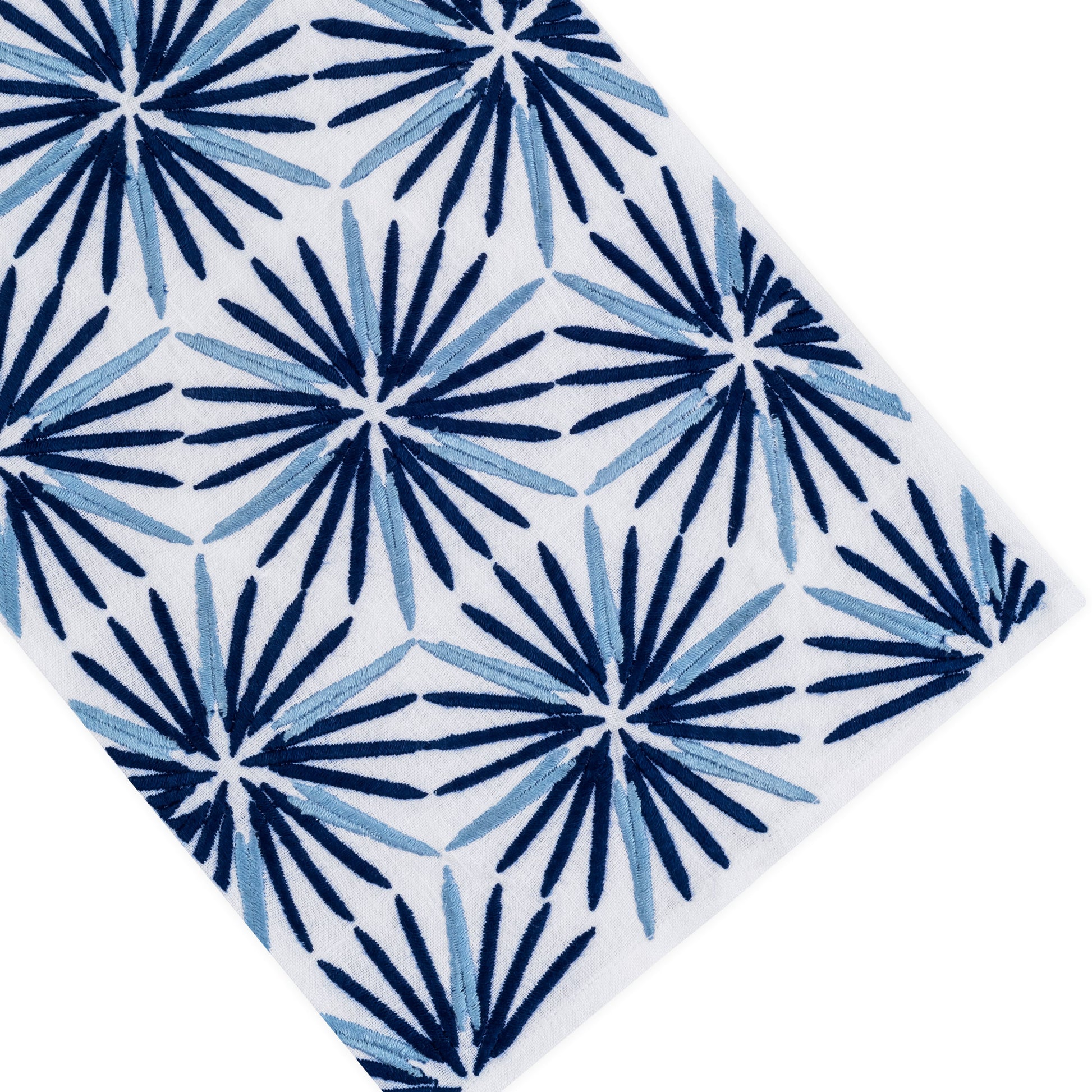 Experience the Radiant Bath Collection by Haute Home—premium white Italian linen adorned with a repeating pattern of blue and navy starburst motifs reminiscent of stylized palm leaves, viewed at an angle; the ideal choice for elevated home décor projects.