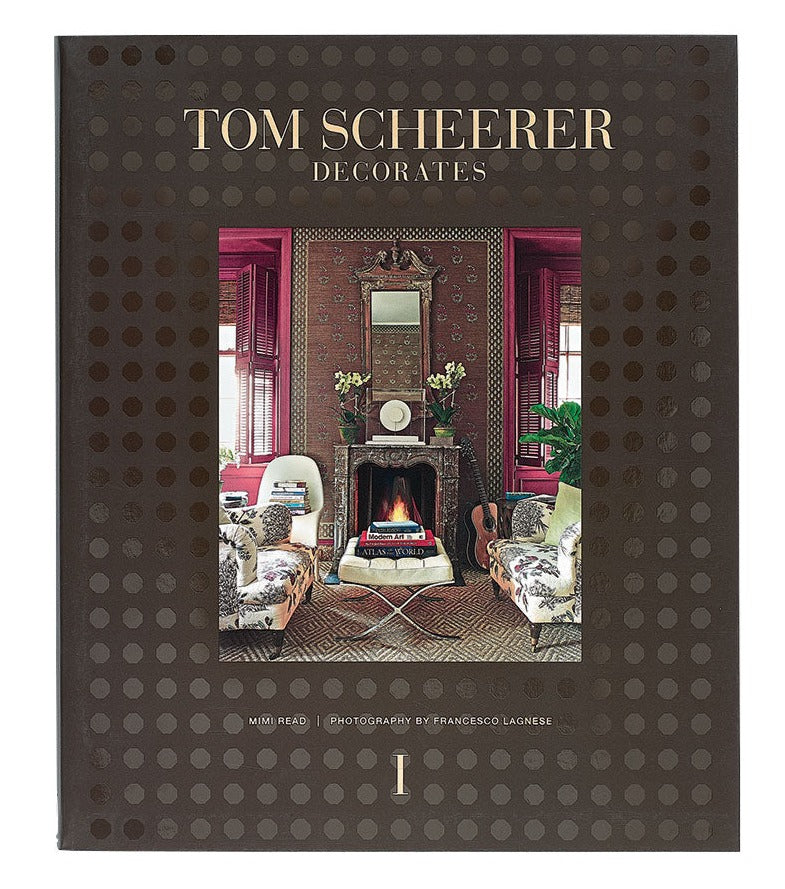 A hardcover book titled "The Tom Scheerer Compendium" by Vendome featuring a cover image of a stylishly decorated living room with a fireplace, patterned furniture, and ornate wall decor, epitomizing Tom Scheerer's relaxed modernism in American interior design.