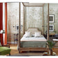 An elegant bedroom featuring a four-poster bed, green armchairs, and floral wallpaper exudes style. Wooden furniture and red curtains add to the decor's warmth. Enhancing the cozy ambiance, a plant and artworks reflect Tom Scheerer's signature blend of relaxed modernism with American interior design elements as illustrated in "The Tom Scheerer Compendium" by Vendome.
