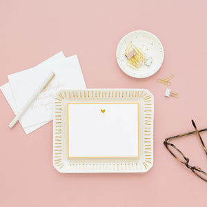 Flat lay of a desk with a blank card on the Sugar Paper Scatter Dot Trinket Tray, pen, paper clips in a dish, envelopes, and eyeglasses on a pink background.