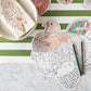 Tabletop featuring the Hester & Cook Die Cut Coloring Turkey Placemat, colored pencils, a striped green and white placemat, a bowl, and a napkin with autumn designs—perfect for a festive holiday crafts coloring activity.
