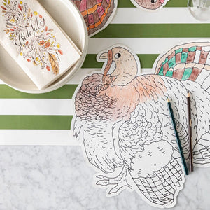 Tabletop featuring the Hester & Cook Die Cut Coloring Turkey Placemat, colored pencils, a striped green and white placemat, a bowl, and a napkin with autumn designs—perfect for a festive holiday crafts coloring activity.