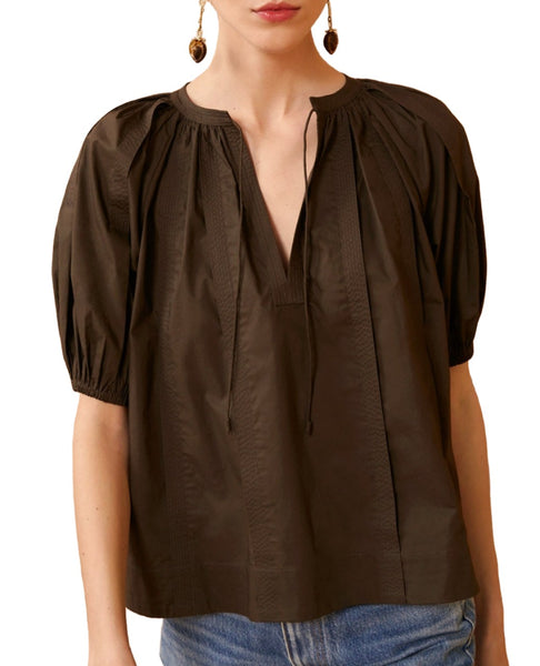 A person wearing an Ulla Johnson Loli Militaire Top, a dark brown, short-sleeved, V-neck blouse with gathered detailing and voluminous puff sleeves, paired with blue jeans.