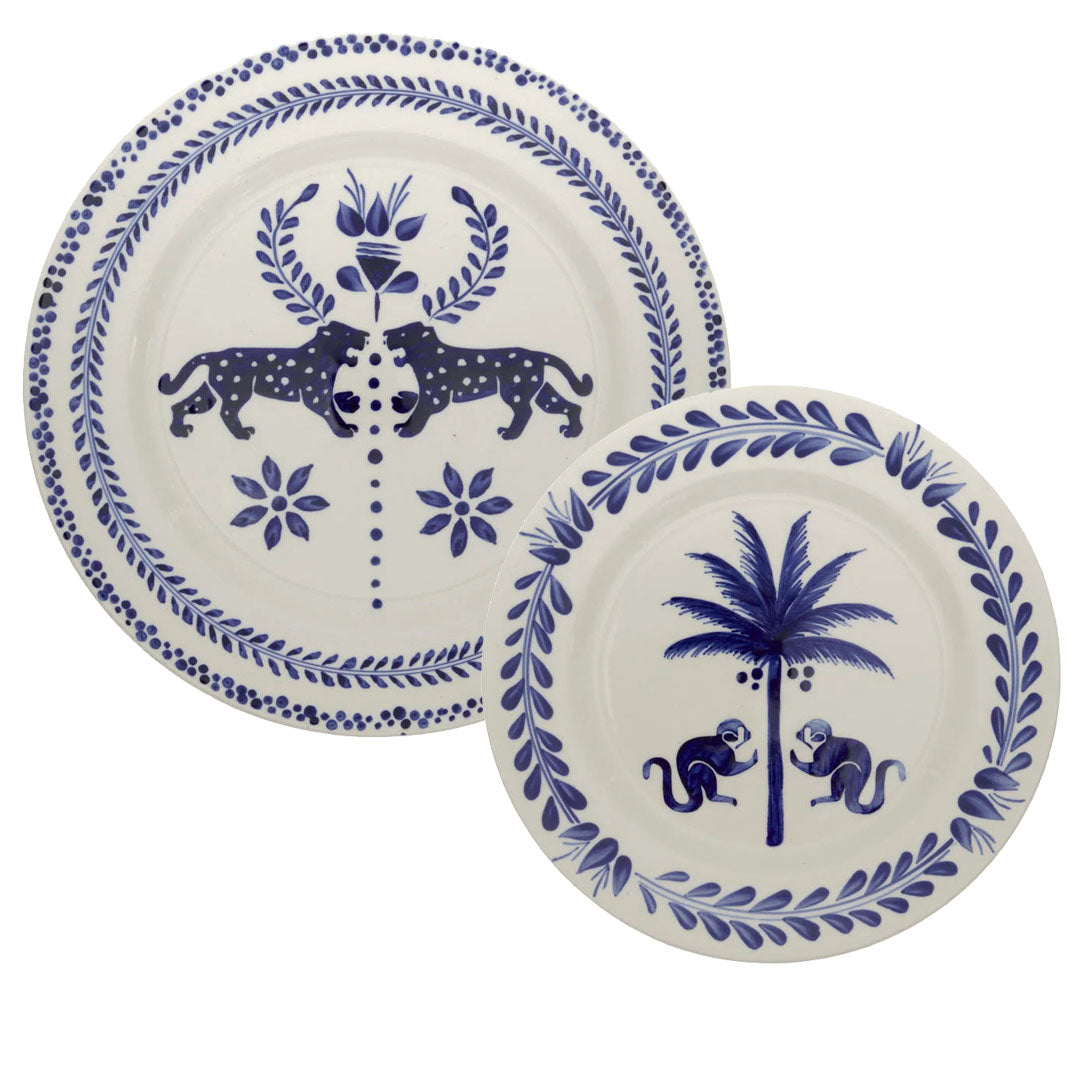 Two hand-painted ceramic plates from the Casa Deep Navy Dinnerware Collection by Johanna Ortiz; one features leopards with a flower, the other shows monkeys and a palm tree. Crafted from Carmen de Viboral clay, they highlight exceptional artisanal heritage.