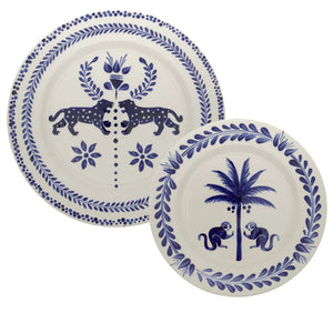 Two hand-painted ceramic plates from the Casa Deep Navy Dinnerware Collection by Johanna Ortiz; one features leopards with a flower, the other shows monkeys and a palm tree. Crafted from Carmen de Viboral clay, they highlight exceptional artisanal heritage.