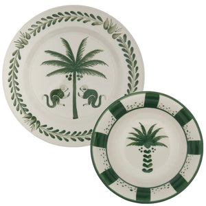 Two ceramic plates from Johanna Ortiz's Casa Dark Jungle Dinnerware Collection: the larger features a palm tree with two monkeys, the smaller has a palm tree and green border—exquisite hand-painted pieces inspired by Carmen de Viboral’s heritage.
