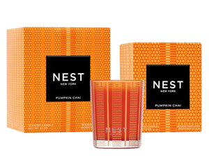 The Pumpkin Chai Candle Collection by Nest features a fragranced votive candle in a glass holder, paired with two matching orange patterned boxes—ideal for adding autumn ambiance to any space.