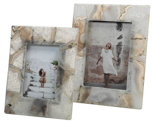 Showcase memories with Zodax's Preto Agate Frame: one displays a seated figure on stairs, the other highlights a standing person in a white dress by a textured wall—each with an elegant stone-patterned design.