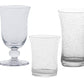 Three clear glasses from the Juliska Provence Basil Drinkware Collection, each with a unique bubbled texture and different shapes and sizes, are displayed against a white background.