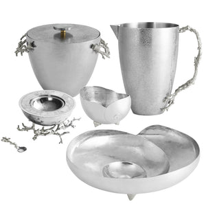 The Michael Aram Ocean Reef Serveware and Barware Collection features five silver and white pieces with textured surfaces and branch-inspired handles, including a pitcher, covered vessel, bowl, dish, and spoon—ideal for coral reef-themed decor.