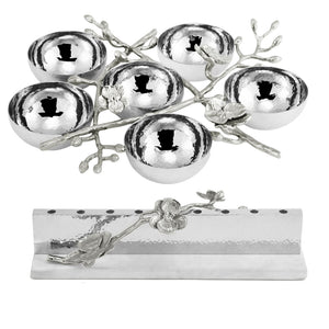 Six silver bowls are arranged on a decorative, branch-like tray with floral accents from the White Orchid Judaica Collection by Michael Aram, accompanied by a matching silver holder featuring an orchid detail.