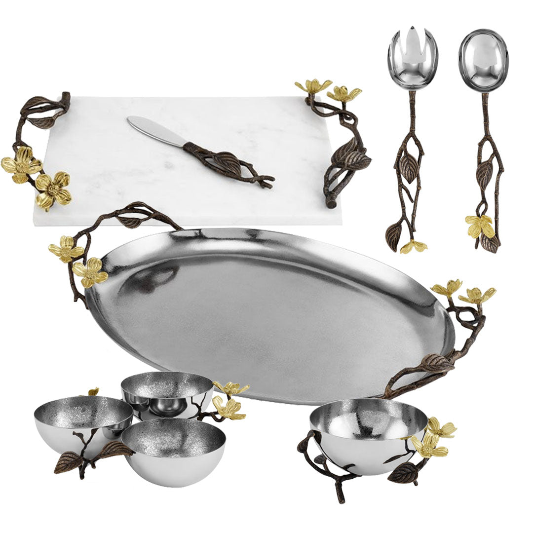 The Michael Aram Dogwood Serveware Collection features a marble cheese board, serving utensils, metal tray, and bowls—all with bronze and gold nature-inspired accents.