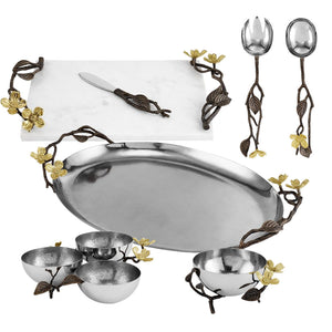 The Michael Aram Dogwood Serveware Collection features a marble cheese board, serving utensils, metal tray, and bowls—all with bronze and gold nature-inspired accents.