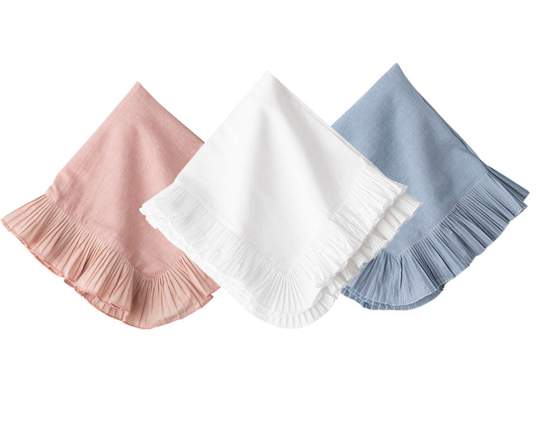 The Juliska Mademoiselle Napkin Set features three folded napkins with knife-pleat ruffle borders in pink, white, and blue, arranged side by side on a white background—ideal for a romantic tablescape.