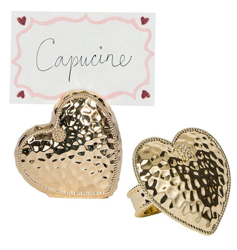 Two Berry & Thread Heart Napkin Rings and Place Card Holders by Juliska, featuring a hammered gold finish and a handwritten "Capucine" card bordered with pink and red hearts.