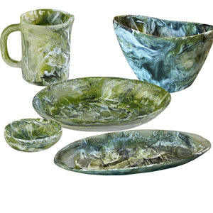 The Nashi Home Serveware Collection, Forest by Nashi Home features five marbled green and white ceramic dishes—a mug, bowl, small bowl, round plate, and oval plate—ideal for serving or elevating your table decor. Displayed on a white background.