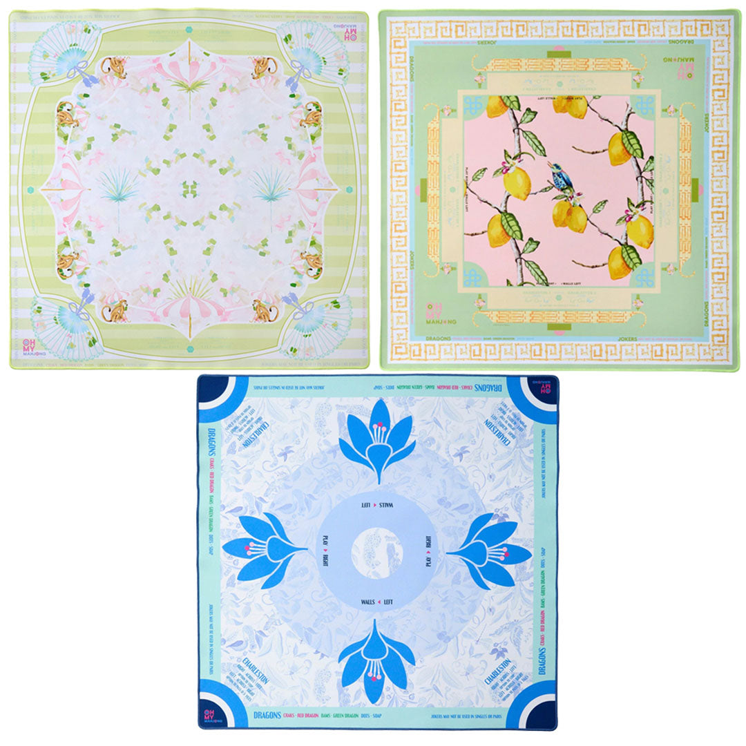 The Oh My Mahjong Mahjong Mat Collection offers three square silk scarves: shells and sea motifs, yellow lemons on pink, and blue flowers with geometric patterns—all inspired by the elegance of their non-slip mahjong mats.