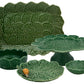 The Hive Geranium Leaf Serveware Collection features green ceramic dishes and trays with leaf patterns—a platter, bowl, cake stand, and plate are shown together. A snail is resting on one of the plates.