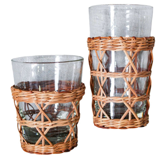 The Seagrass Rattan Cage Tumbler Collection by Be Home features two clear glass tumblers with woven wicker sleeves, blending rustic charm and modern style—shown side by side in different heights.