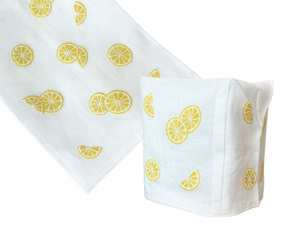 From Haute Home's Lemon Slice Bath Collection: a white Italian linen cloth and fabric tissue box cover, both featuring hand-embroidered yellow lemon slice motifs.