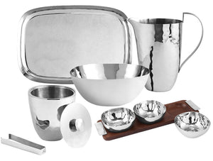 The Michael Aram Reflective Serveware Collection features high-polished stainless steel pieces—tray, pitcher, bowl, ice bucket with lid and tongs, and small bowls on a wooden tray—ideal for lovers of modern design.