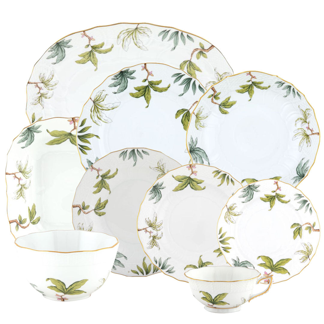 The Herend Foret Garland Collection features white artistic porcelain dishes, bowls, and teacups with green botanical patterns and gold trim, beautifully arranged together.