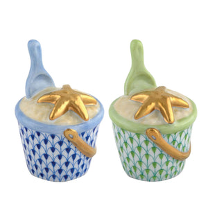 The Beach Bucket Collection by Herend features two small hand-painted ceramic containers with handles and spoons, decorated in blue and green with gold starfish lids, crafted in the style of fine white porcelain.