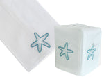 The Haute Home Playful Starfish Bath Collection in Aqua features a white linen napkin and tissue box cover, both adorned with blue hand-embroidered starfish designs.