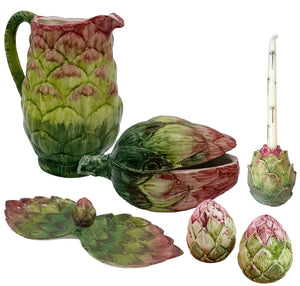 The Les Ottomans Artichoke Decor and Serveware Collection includes a hand-painted Italian ceramic pitcher, serving spoon, candle holder with candle, leaf-shaped dish, and two small bowls.