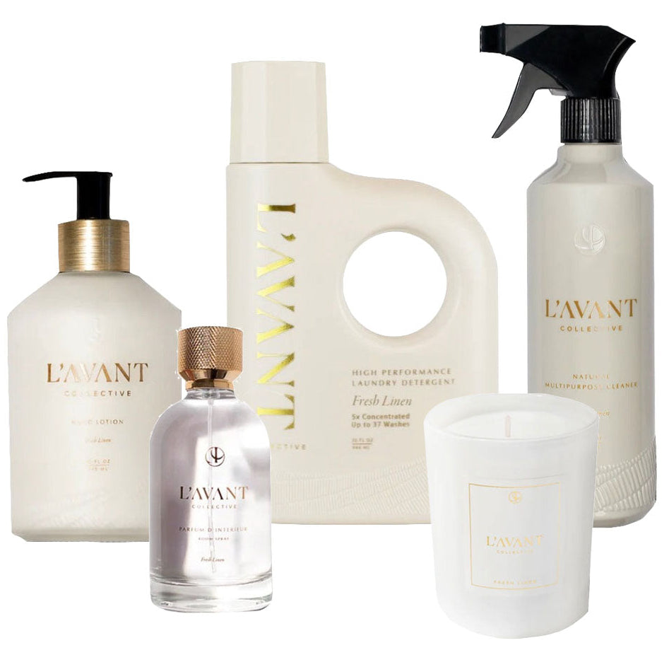 Five L'Avant Collective Fresh Linen Scent Collection products—hand soap, laundry detergent, spray cleaner, room spray, and a white candle—are displayed together against a plain white background.