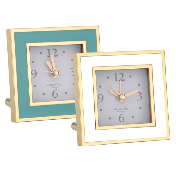 The Addison Ross Gold Square Alarm Clock Collection features two square clocks with gold frames and silent sweep movement. One has a teal border, the other a white border, both displaying "Addison Ross London." A luxury velvet back enhances their exquisite design.